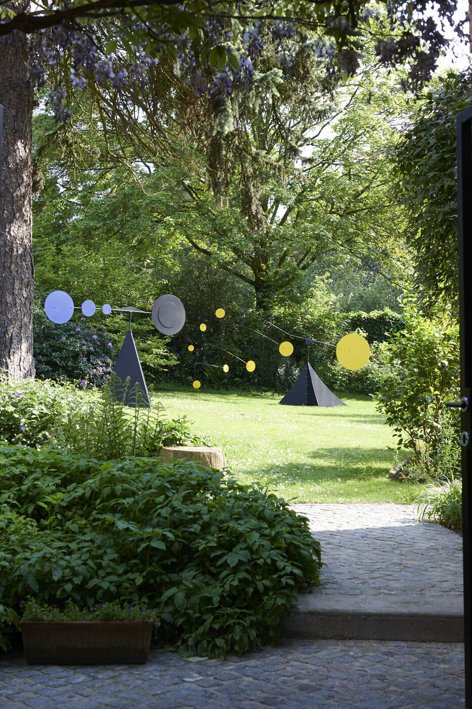 Vue à travers une grille de jardin vers les mobiles Pyramide et Alfredo exposés sur une pelouse